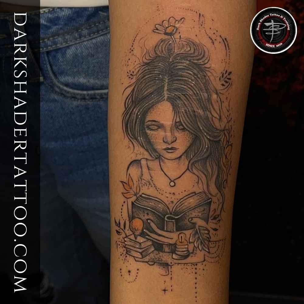 A tattoo of a girl reading a book with floral, light, and leaf designs on a girl’s hand, showcasing a creative and artistic design. this is one of the best tattoos for girls
