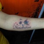 "Nandkishor" calligraphy tattoo with butterfly and love icons, designed by the best tattoo artist in Kolkata at Dark Shader Tattoo.